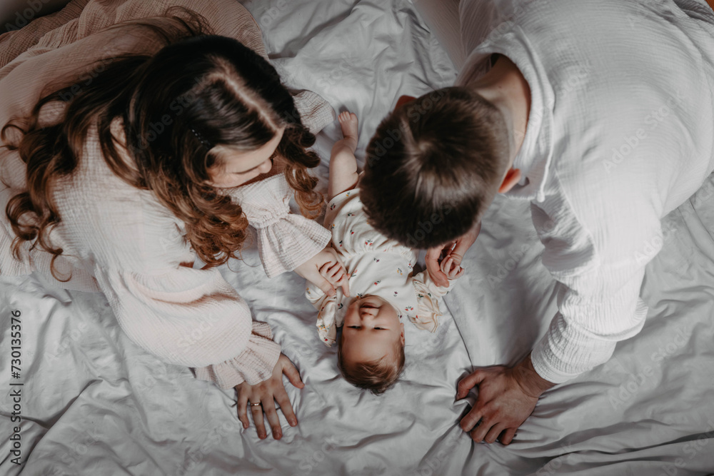 Parents with baby lying on white bed at home in the morning