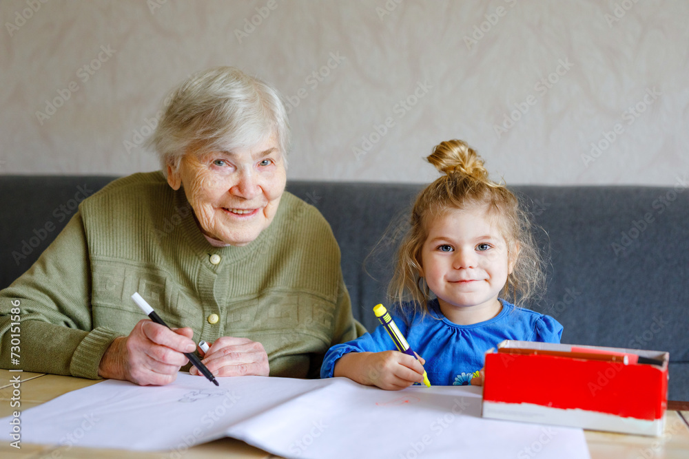 Beautiful toddler girl and grand grandmother drawing together pictures with felt pens at home. Cute child and senior woman having fun together. Happy family indoors Beautiful toddler girl and grand grandmother drawing together pictures with felt pens at home. Cute child and senior woman having fun together. Happy family indoors