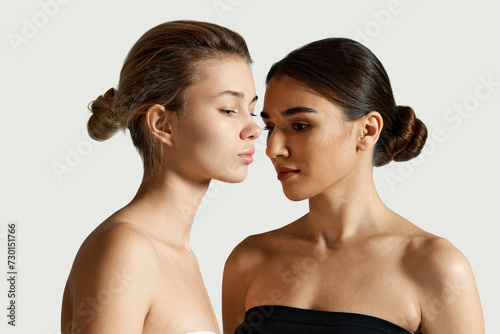 Two beautiful girls with natural makeup, perfect, well-kept smooth skin posing against white studio background. Concept of natural beauty, cosmetology and cosmetics. Skincare product advertisement