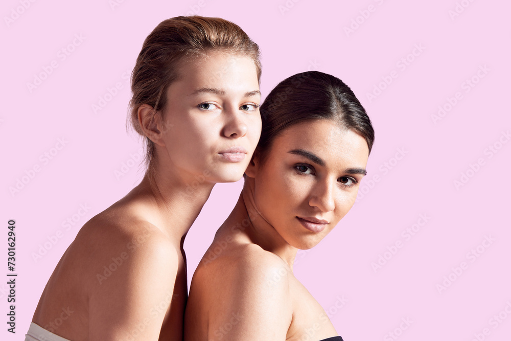Portrait of beautiful brunette and blonde girls with well-kept skin, nude makeup, bare shoulders against pink studio background. Concept of natural beauty, cosmetology and cosmetics, skincare Portrait of beautiful brunette and blonde girls with well-kept skin, nude makeup, bare shoulders against pink studio background. Concept of natural beauty, cosmetology and cosmetics, skincare