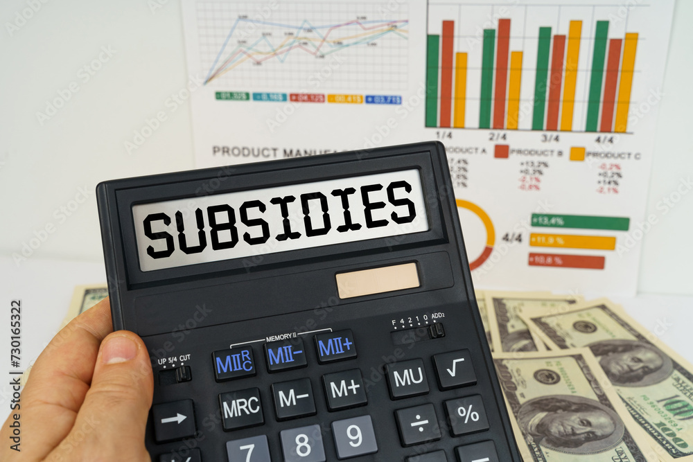 On the table there are financial reports, dollars, in the hands of a calculator with the inscription - Subsidies On the table there are financial reports, dollars, in the hands of a calculator with the inscription - Subsidies