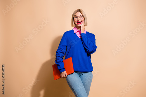 Photo of astonished pretty girl hold laptop unexpected reaction empty space isolated on beige color background