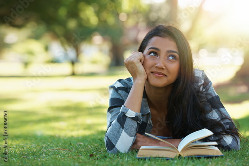 Happy woman, student and thinking with book for reading, literature or studying on green grass. Young or thoughtful female person with smile in wonder for chapter, learning or outdoor story in nature