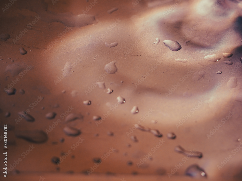 Fototapeta premium Water drops on silver aluminum background with brown reflections for a mysterious abstract background.