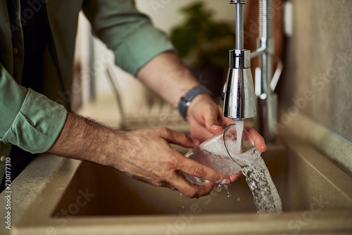 A man washing cup and rinse it with running water in the kitchen sink.