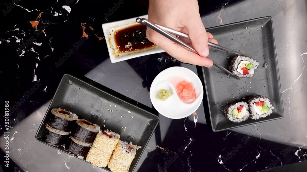 Close up of hands with chopsticks eating japanese food. Traditional asian rolls. Maki sushi with vegetables and tuna. Wasabi and Soy Sauce in bowl. Close up of hands with chopsticks eating japanese food. Traditional asian rolls. Maki sushi with vegetables and tuna. Wasabi and Soy Sauce in bowl.