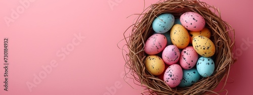 colorful easter eggs in a nest on pastel pink background, banner with copyspace, top view photo