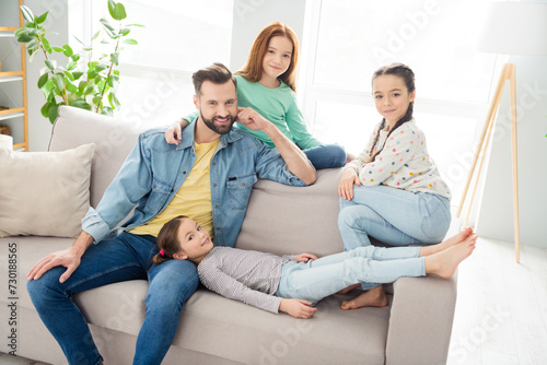 Portrait of four persons cheerful man sit o f sofa with adorable positive girls enjoy free time weekend home indoors photo