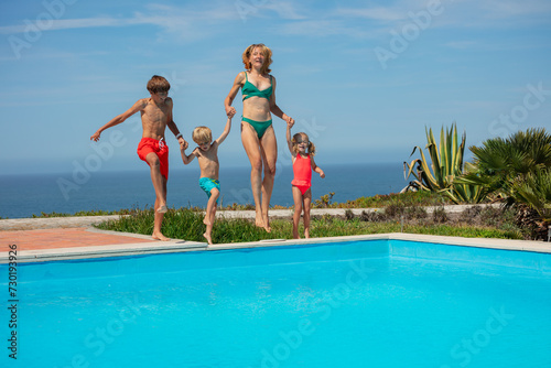 Beautiful family in motion by pool, laugh and jump together