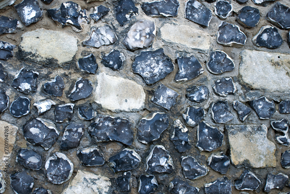 Detailed close-up of aged and weathered rough-hewn flint cobblestone wall texture with various shapes and colors, natural stone surface background for architectural and design projects Detailed close-up of aged and weathered rough-hewn flint cobblestone wall texture with various shapes and colors, natural stone surface background for architectural and design projects