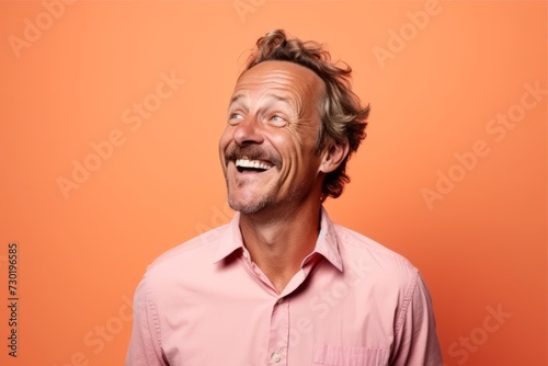 Cheerful middle age man in pink shirt over orange background. © Iigo