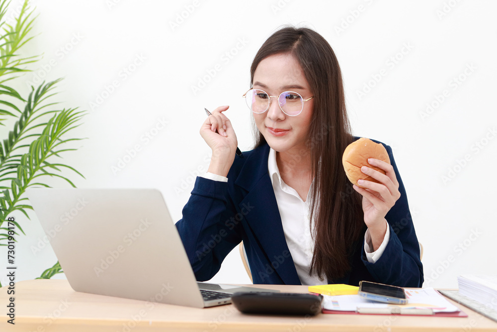 An Asian female employee wearing a suit and eyeglasses is eating breakfast while sitting and working. Business concept. An Asian female employee wearing a suit and eyeglasses is eating breakfast while sitting and working. Business concept.