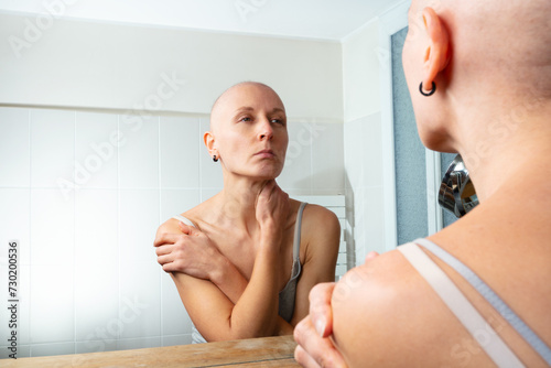 Contemplating woman ill of cancer facing her image without hair