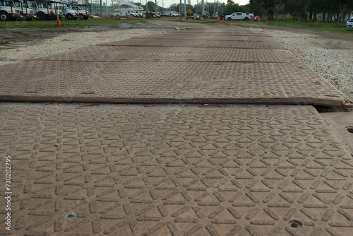 Construction temporary road access mats low angle view across the grass for Protection from heavy loads. Wide shot over tan mats with triangles afternoon sun in Florida. Dirt and grass on sides.