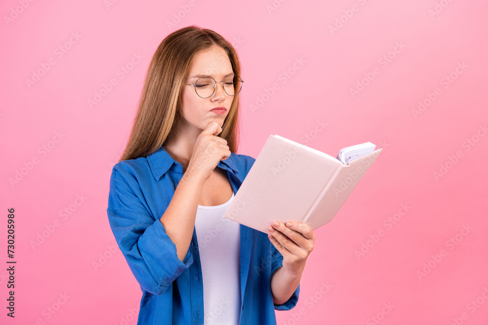 Photo of doubtful unsure girl wear blue shirt arm hand chin reading book empty space isolated pink color background Photo of doubtful unsure girl wear blue shirt arm hand chin reading book empty space isolated pink color background