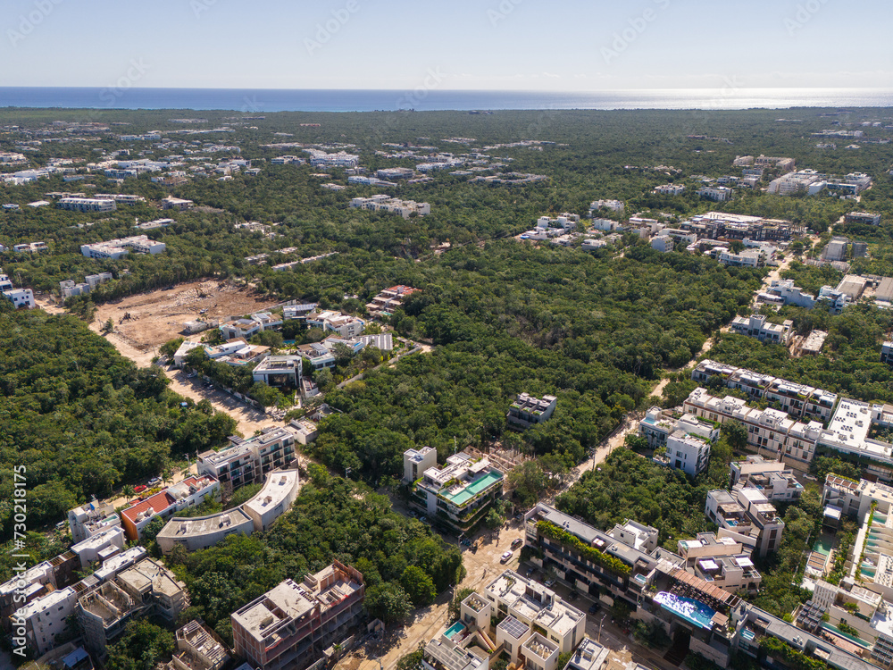 Drone view of streets surrounded by green tropical vegetation with Caribbean Sea and cloudless blue sky in the background in Tulum on a sunny day 
