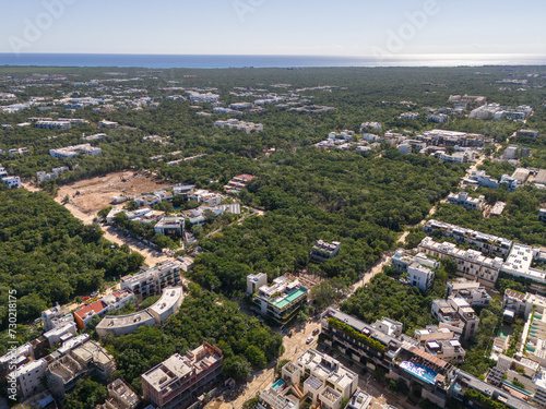 Drone view of streets surrounded by green tropical vegetation with Caribbean Sea and cloudless blue sky in the background in Tulum on a sunny day 