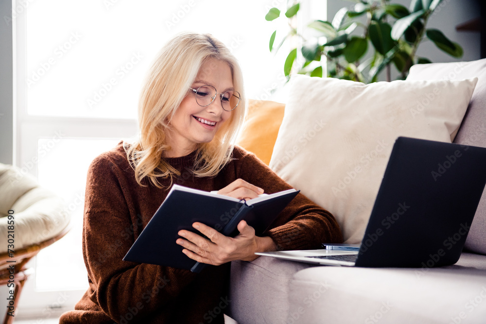 Photo of cheerful charming senior woman sitting on floor writing notes in notepad video lesson conference webinar Photo of cheerful charming senior woman sitting on floor writing notes in notepad video lesson conference webinar