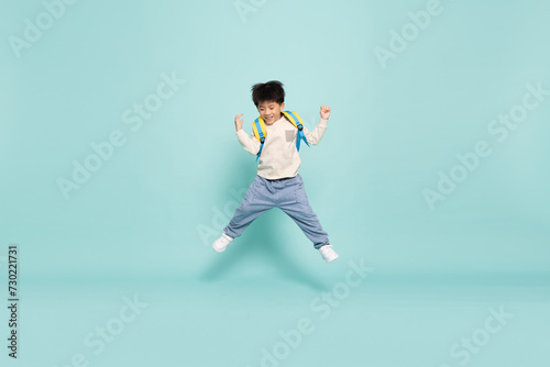 Asian little boy jumping and carries a backpack to school in casual clothes isolated on green background, Back to school concept