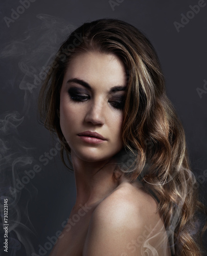 Woman, eyeshadow and makeup, beauty and smoke with hair, cosmetics and balayage on grey background. Serious model, edgy with haircare and vapor, cosmetology and skin with mist or fog in studio