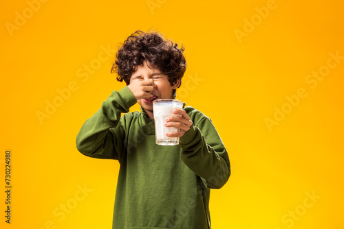 Lactose intolerance. Dairy intolerant child boy holding glass of milk over yellow background. photo