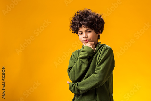 Thoughtful child boy holds chin on yellow background. Dreaming concept photo