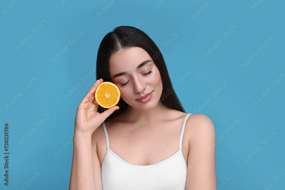 Beautiful young woman with piece of orange on light blue background Beautiful young woman with piece of orange on light blue background