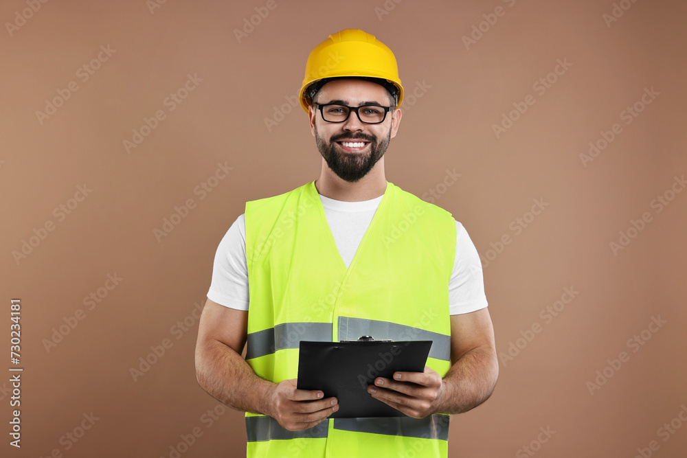 Engineer in hard hat holding clipboard on brown background Engineer in hard hat holding clipboard on brown background