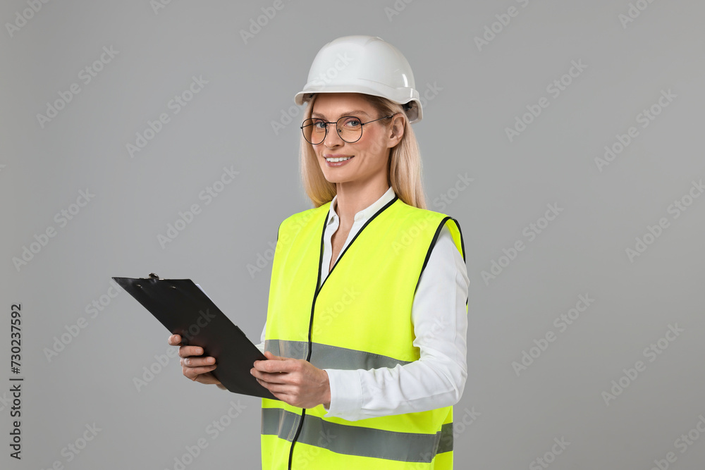 Engineer in hard hat holding clipboard on grey background Engineer in hard hat holding clipboard on grey background