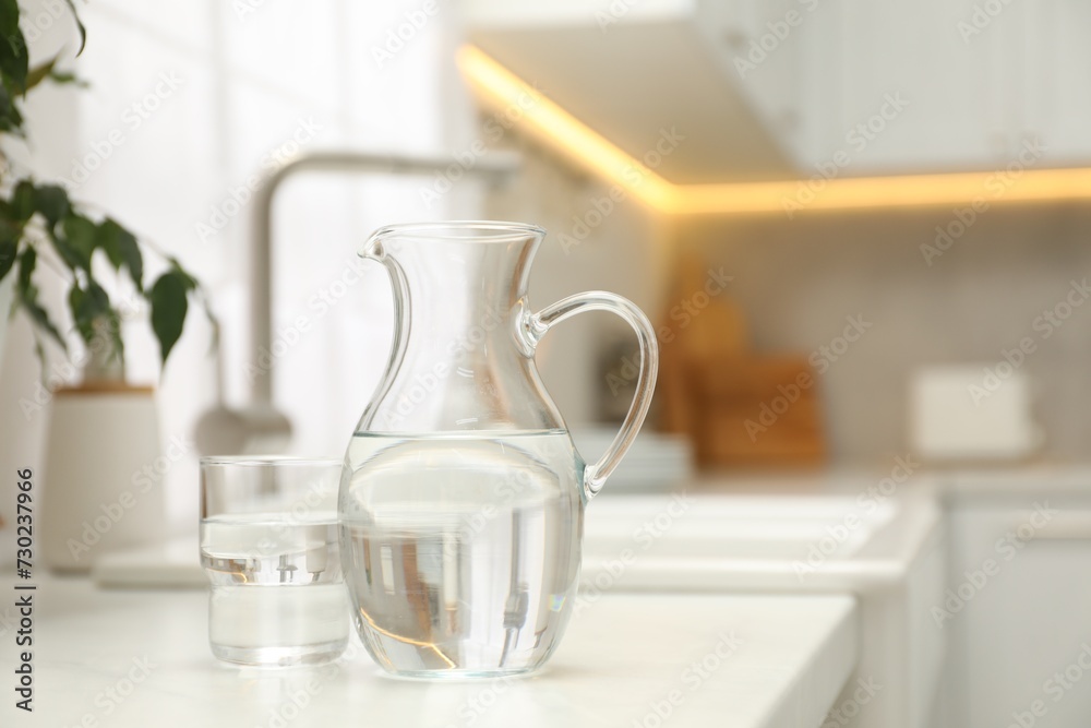 Jug and glass with clear water on white table in kitchen, space for text Jug and glass with clear water on white table in kitchen, space for text