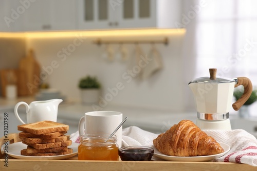 Breakfast served in kitchen. Toasts  honey  jam  fresh croissant  coffee and pitcher of milk in wooden tray  closeup