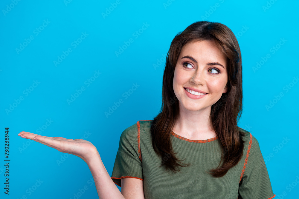 Portrait of positive lovely lady beaming smile look arm hold empty space offer isolated on blue color background Portrait of positive lovely lady beaming smile look arm hold empty space offer isolated on blue color background