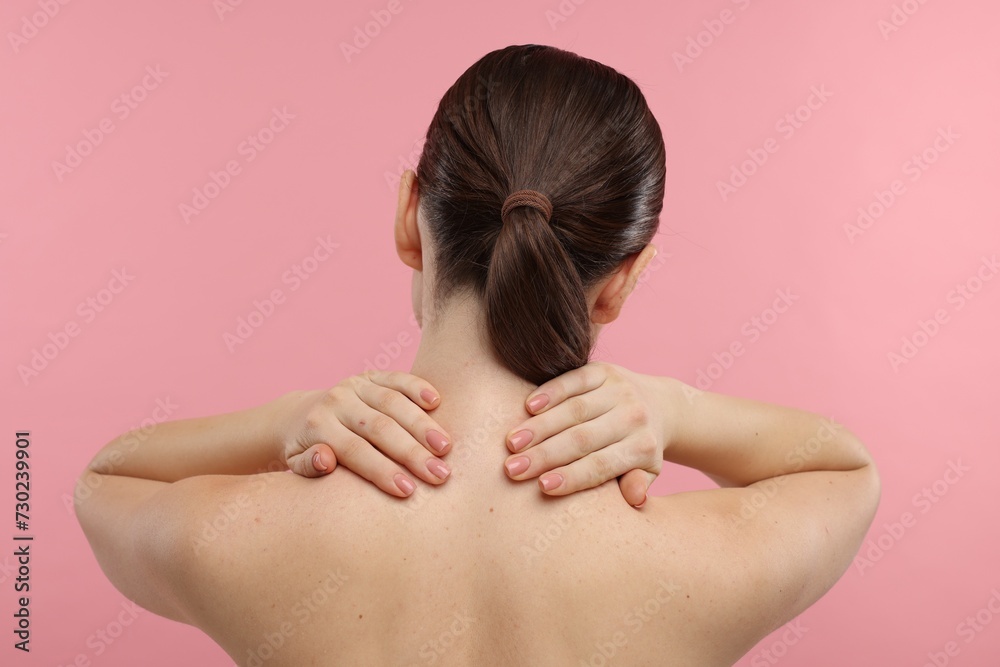 Woman touching her neck on pink background, back view Woman touching her neck on pink background, back view