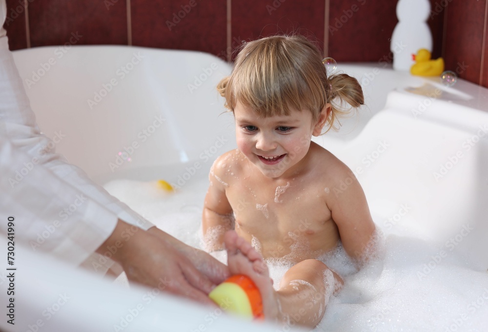 Mother washing her smiling daughter with sponge in bathtub, closeup Mother washing her smiling daughter with sponge in bathtub, closeup