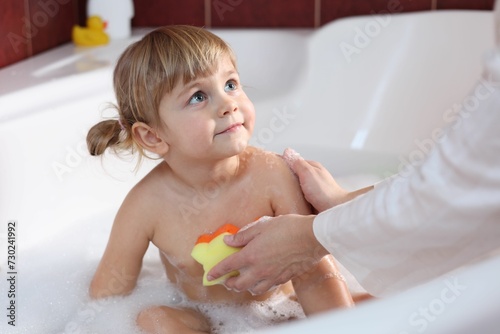 Mother washing her little daughter with sponge in bathtub, closeup
