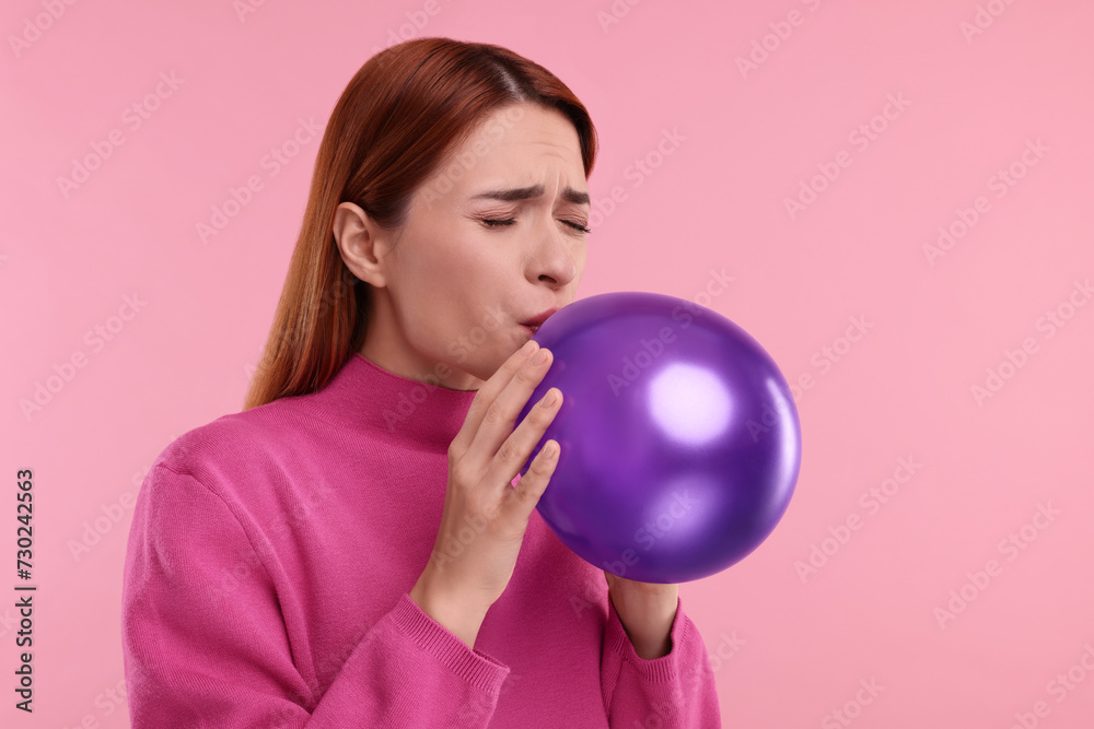 Woman inflating purple balloon on pink background Woman inflating purple balloon on pink background