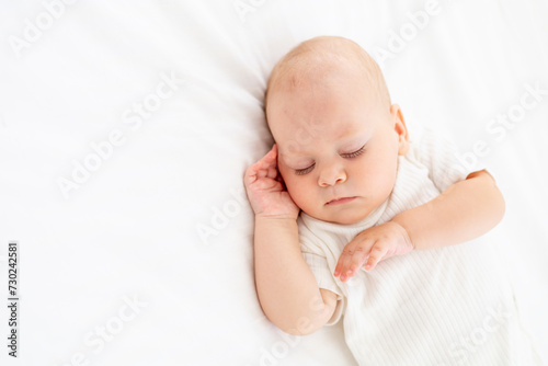 cute little newborn baby sleeps with his hand folded under his cheek, sweet healthy baby sleep in a white crib, a place for text