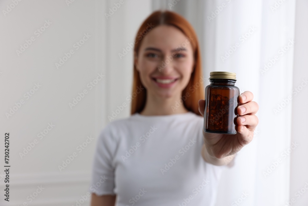 Beautiful young woman with jar of vitamin pills at home, selective focus Beautiful young woman with jar of vitamin pills at home, selective focus