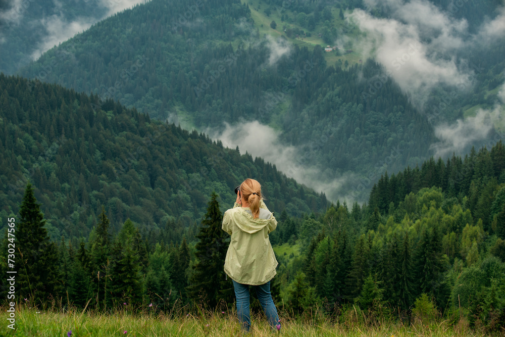 A girl tourist photographs a foggy mountain landscape.