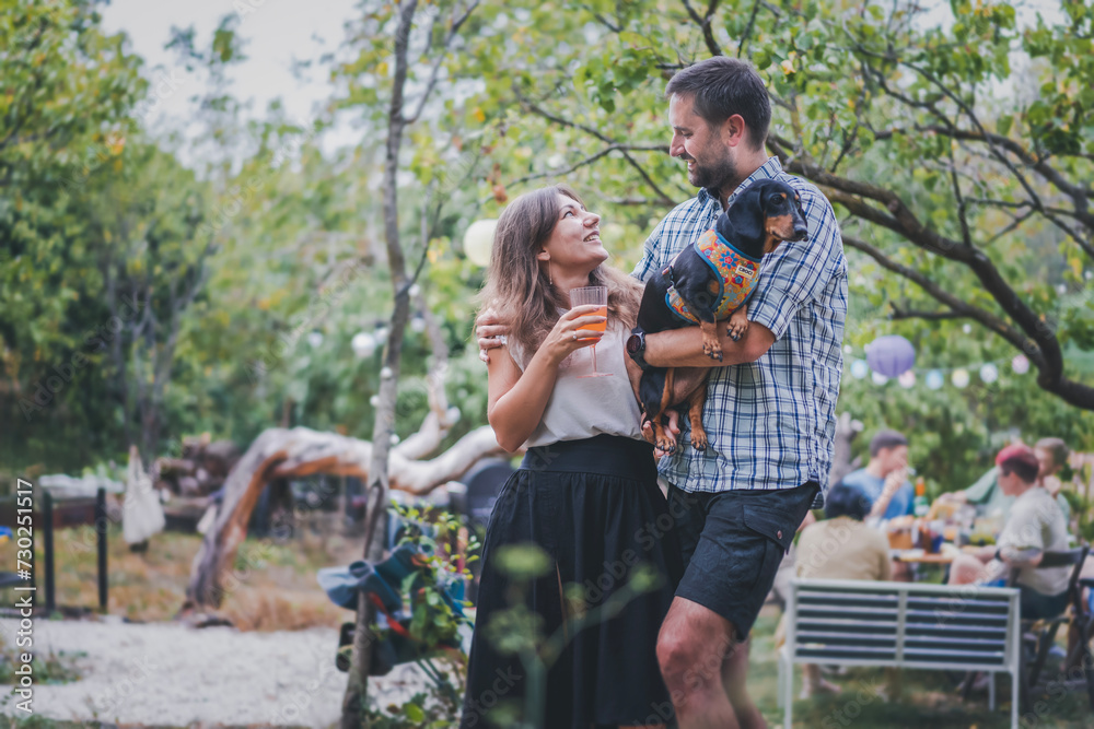 Fototapeta premium Young attractive romantic happy Caucasian couple with their pet dachshund dog spending time together during a garden party. Love concept