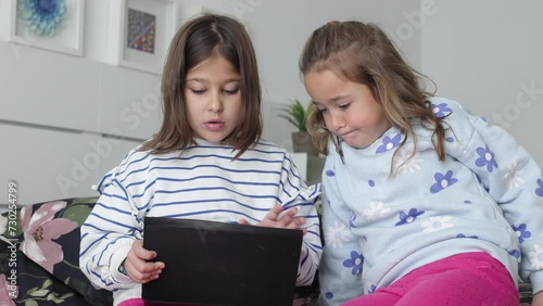 Two sisters looking at a tablet, sitting on a camera. Concept of play, learning, having fun, sharing, together and twins.