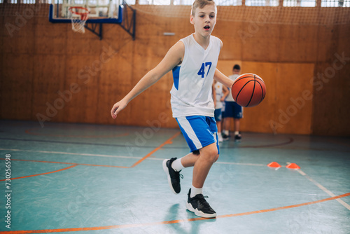 A young basketball kid in action dribbling a ball on court on training. © Zamrznuti tonovi