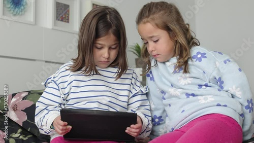 Two sisters looking at a tablet, sitting on a camera. Concept of play, learning, having fun, sharing, together and twins.