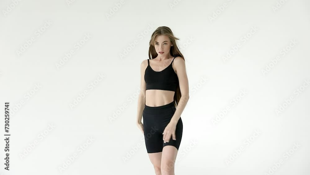 A beautiful slender girl in black leggings and a top with her hair down poses in a white studio. Slow motion A beautiful slender girl in black leggings and a top with her hair down poses in a white studio. Slow motion