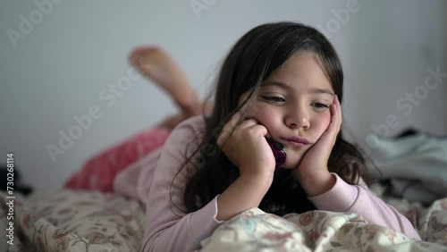 One bored little girl feeling extreme boredom with nothing to do laid in bed with hands in chin. Sad contemplative 8 year old child close-up face