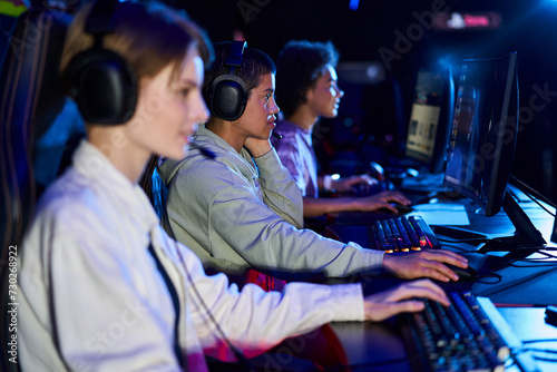 Diverse and young interracial women engaged in cybersport games, using computers and headphones