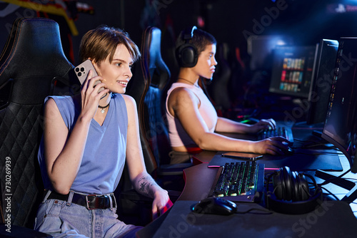 woman sitting at a computer desk talking by phone near friend playing in computer game in club