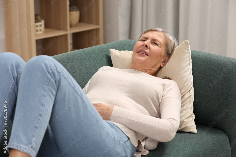 Menopause. Woman suffering from abdominal pain on sofa at home Menopause. Woman suffering from abdominal pain on sofa at home
