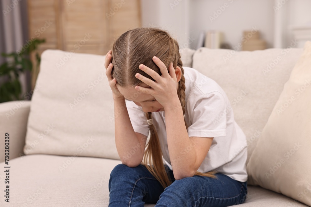 Little girl suffering from headache on sofa indoors Little girl suffering from headache on sofa indoors