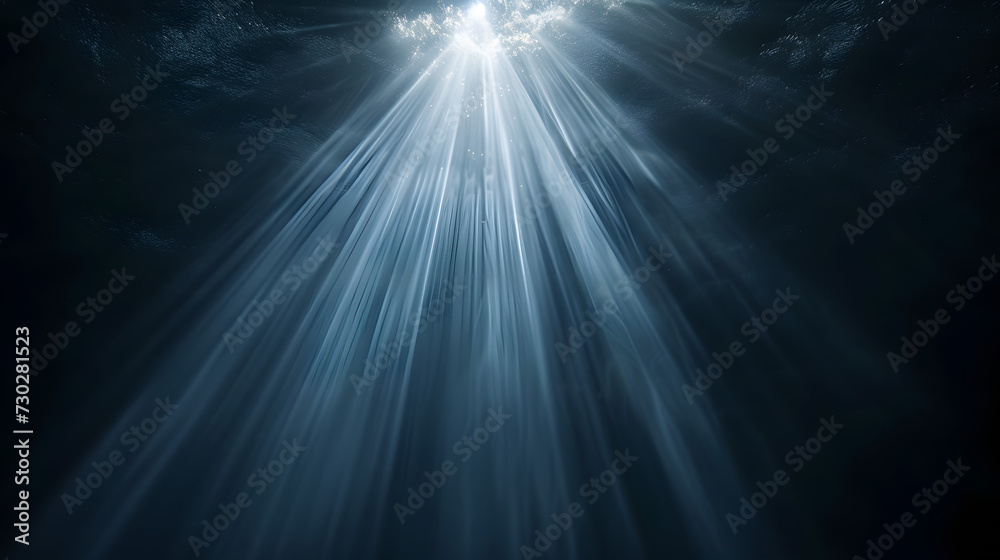 Sun rays and light shining through surface of ocean seen from underwater on black background